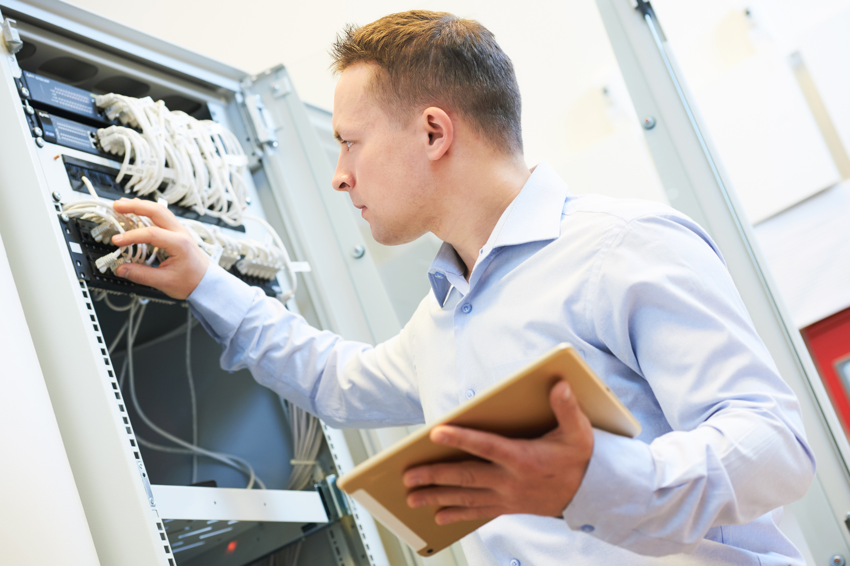 Ein Mann mit einem Tablet in einer Hand, hantiert mit der anderen Hand an einem Server herum / Datenschutz