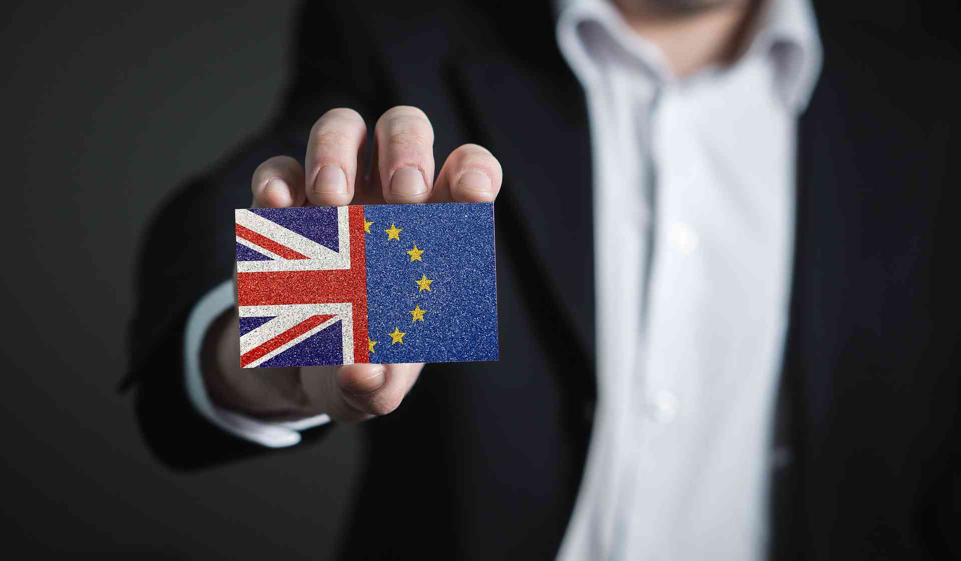 Datenschutz im Brexit. Ein Mann im Anzug hält einen Gegenstand nach vorne auf dem die UK- und EU-Flaggen abgebildet sind.
