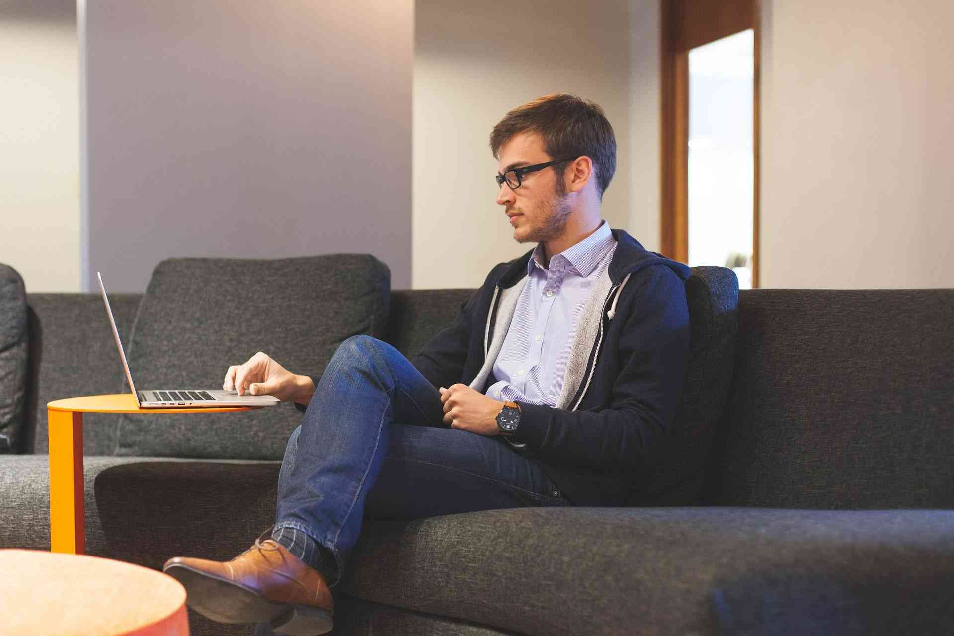 Mann im Homeoffice am Laptop auf dem Sofa mit Datenschutz beschäftigt.